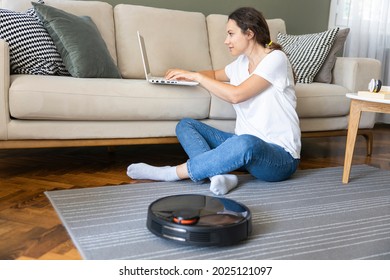 aspiradora de robots limpiando la sala de estar. Mujer joven disfruta de descansar sentada en el sofá de su casa