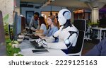 Robot working at computer among people. Maschine typing on keyboard in office. IT team of future. Futuristic worker. Humanoid work at call center. Support job. Selling concept. Technologies.