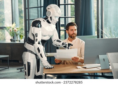 Robot and young businessman working at a computer in a modern office. Collaboration between humans and artificial intelligence. - Powered by Shutterstock