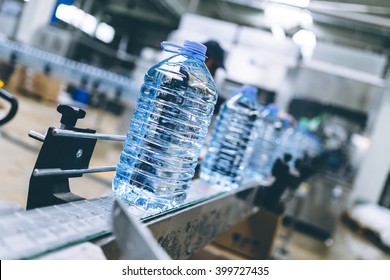 Robotic factory line for processing and bottling of pure spring water into canisters and bottles. Unrecognizable worker in background. Selective focus.