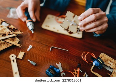 Robotic school project: Young student building robot vehicle at artificial intelligence programming class - STEM education concept - Focus on right hand holding wood piece