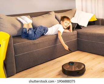 Robotic vacuum cleaner clean floor, while boy playing with tablet computer on the sofa. Child easily controlling vacuum cleaner with remote control. Smart home, housework, cleaning technology concept. - Powered by Shutterstock
