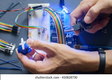 Robotics development closeup., electronic invention. Engineer, programmer, inventor hands with special cables, wires, working with breadboard and constructing robot at home. Modern technologies. Hobby