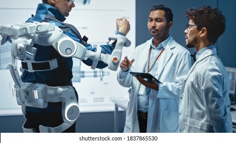 In Robotics Development Laboratory: Engineers and Scientists Work on a Bionics Exoskeleton Prototype with Person Testing it. Designing Wearable Exosuit to Help Disabled People.
