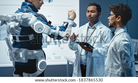 In Robotics Development Laboratory: Engineers and Scientists Work on a Bionics Exoskeleton Prototype with Person Testing it. Designing Wearable Exosuit to Help Disabled People.