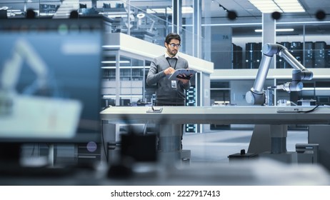 Robotics Engineer Researching and Developing a Technological Robot Arm Project, Standing with Tablet Computer in Scientific Technology Lab. Young Male Working on an AI Robotic Arm.