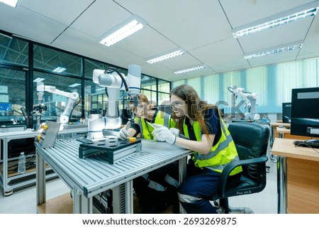 A robotics engineer uses a tablet to program a robot with a machine vision system, while her colleague calibrates the end-of-arm tooling on another unit in a system integration lab.