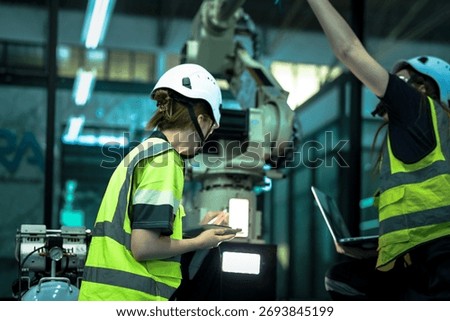 A robotics engineer uses a tablet to program a robot with a machine vision system, while her colleague calibrates the end-of-arm tooling on another unit in a system integration lab.