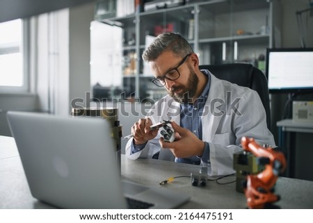 Robotics engineer working on desing of modern robotic arm adn sitting at dest in laboratory.