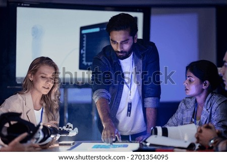 A robotics engineering team in an RD lab reviews a prototype. They are designing an AI powered robotic arm, analyzing data on a screen and a smart table.