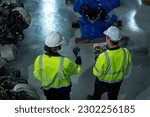 Robotics engineers using tablet inspect and designing modern robotic arm in factory.
