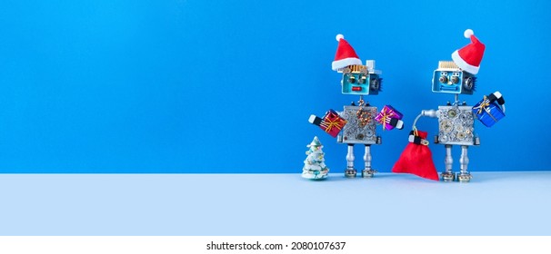 Robotics Greeting Festive New Year Christmas Flyer Card. Two Mechanical Robots, Santa Claus Hats, Toy Tree Gifts. Blue Background Copy Space