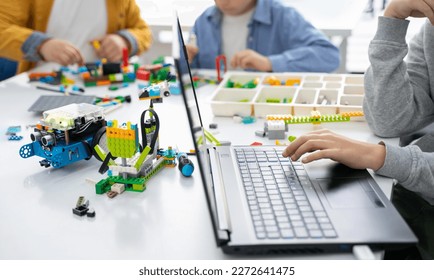 Robotics programming class. Children construct and code Robot. STEM education using constructor blocks and laptop, remote control joystick. Technology educational development for school kids