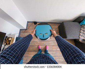 Robots Takeover, Robots As Pets And Evil Robots Concept. Man Holding A Robot Vacuum Cleaner With Eyes And Teeth.