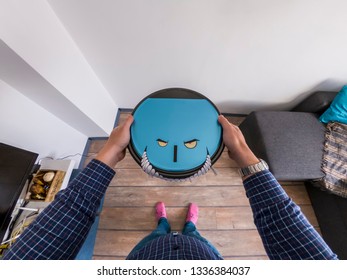 Robots Takeover, Robots As Pets And Evil Robots Concept. Man Holding A Robot Vacuum Cleaner With Eyes And Teeth.