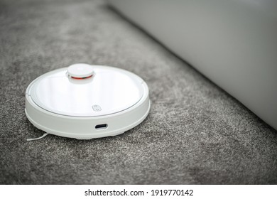 Robots Vacuums Cleaners On Carpet In Living Room For Cleaning Pet Hair And Dust. Vacuuming Robot Working On A Carpeted Surface.