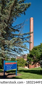 ROCHESTER, MN - 27 JUL 2020: Tall Classic Brick Chimney Smoke Stack At St Marys Hospital, Partially Blocked By Green Trees, And A Mayo Clinic Sign, On A Sunny Summer Day With Clear Blue Sky.