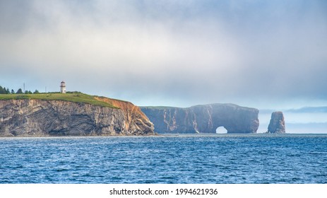 Percé Rock In The Background Of A Lighthouse And The Coast Cliffs, Percé, Quebec, Canada