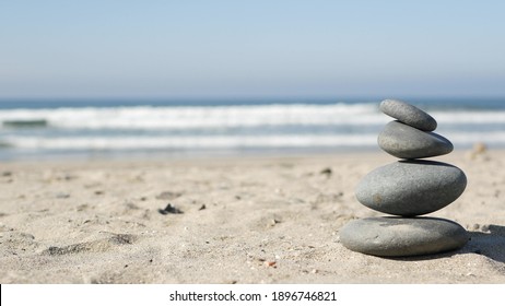 Rock balancing on ocean beach, stones stacking by sea water waves. Pyramid of pebbles on sandy shore. Stable pile or heap in soft focus with bokeh, close up. Zen balance, minimalism, harmony and peace