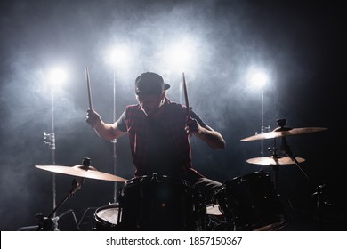 Rock Band Member Playing Drums While Sitting At Drum Kit With Backlit And Smoke On Background