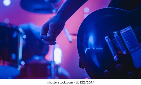 Rock Band Performing at a Concert in a Night Club. Close Up Shot of a Musician Holding and Dropping a Guitar Pick. Live Music Party in Front of Bright Colorful Strobing Lights on Stage.