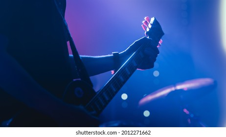 Rock Band Performing at a Concert in a Night Club. Close Up Shot of a Five String Bass Guitar Played by a Musician. Live Music Party in Front of Bright Colorful Strobing Lights on Stage.