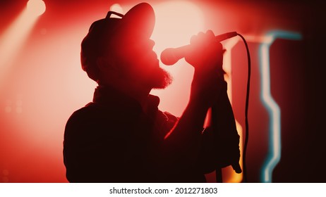 Rock Band Performing at a Concert in a Night Club. Portrait of a Lead Singer Singing into Microphone. Live Music Party in Front of Bright Colorful Strobing Lights on Stage.