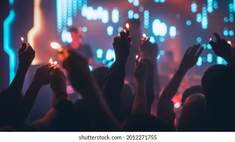 Rock Band Performing a Slow Song at a Concert in a Night Club. Front Row Crowd is Holding Lighters. Silhouettes of Fans Raise Hands in Front of Bright Colorful Strobing Lights on Stage. - Powered by Shutterstock