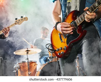 Rock band performs on stage. Guitarist, bass guitar and drums. Guitarist in the foreground. Close-up. - Powered by Shutterstock