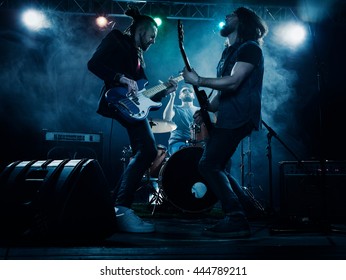 Rock band performs on stage. Guitarist, bass guitar and drums. The guitarist plays solo. - Shutterstock ID 444789211