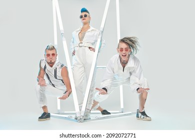Rock band of three charismatic musicians posing in white concert costumes among neon lights. Futuristic space and cybepunk style. Youth alternative culture. Full length portrait.