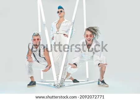Rock band of three charismatic musicians posing in white concert costumes among neon lights. Futuristic space and cybepunk style. Youth alternative culture. Full length portrait.