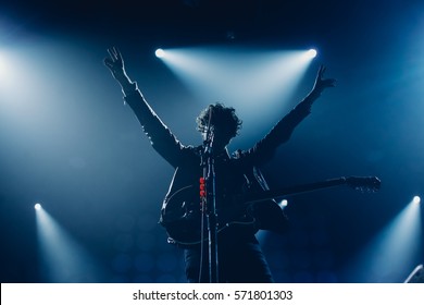 Рок-группа вокалист силуэт с гитарой, пение к микрофону с поднятыми руками в синих огнях