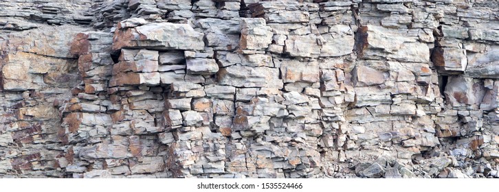 Rock cliff face background. Dangerous vertical wall with protruding crumbling layered stone blocks in quarry for the extraction of wild stone. Abstract texture for stone mining industry