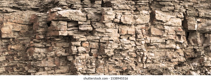 Rock cliff face background. Toned. Wild stone protruding crumbling layered blocks in quarry. Abstract texture for stone mining industry. Copy space for custom text. Front view