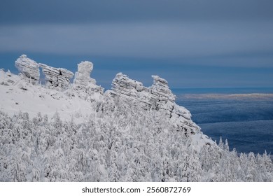 Rock cliff in winter forest is completely covered with hoarfrost. Mystical dawn in the snow-covered mountains. Natural stone statues, rock pillars, weathering posts. - Powered by Shutterstock