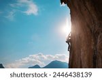 Rock climber climbing rock, man doing olympic sport on natural terrain, strength and endurance training, rock climber on the background of high mountains and blue sky