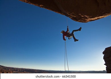 Rock climber dangles in midair as she  rappells past an overhang. - Powered by Shutterstock