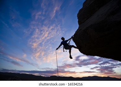 A rock climber is silhouetted against the evening sky as he rappels past an overhang in Joshua Tree National Park. Foto de stock