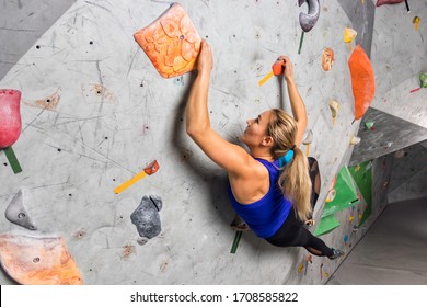 Rock climber woman hanging on a bouldering climbing wall, inside on colored hooks - Shutterstock ID 1708585822