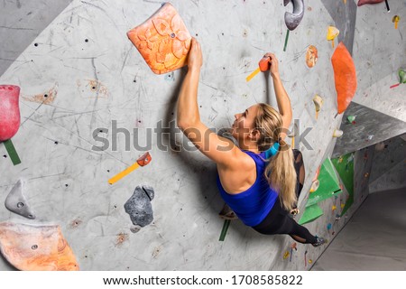 Rock climber woman hanging on a bouldering climbing wall, inside on colored hooks