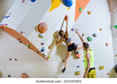 Rock climbers in climbing gym. Young woman climbing bouldering problem (route), man giving her instructions. - Powered by Shutterstock