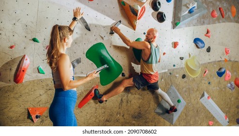 Rock Climbing Instructor Giving Lesson to a Beginner on a Bouldering Wall in a Gym. Female Athlete Holding Tablet Computer and Showing Correct Climbing Techniques to Strong Fit Male. - Powered by Shutterstock