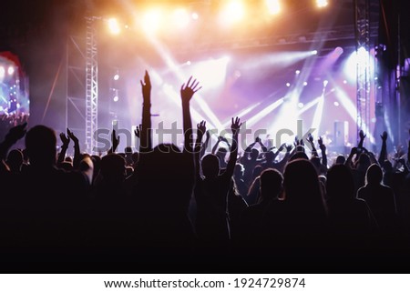 Rock concert, cheering crowd in front of bright colorful stage lights, Hands up with pleasure from the show