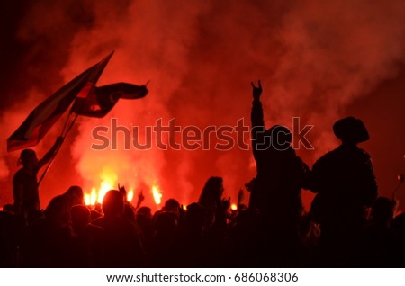 A rock concert in Russia. The outlines of the audience, flags in the light of fireworks. Two silhouettes in the foreground. A bright red glow