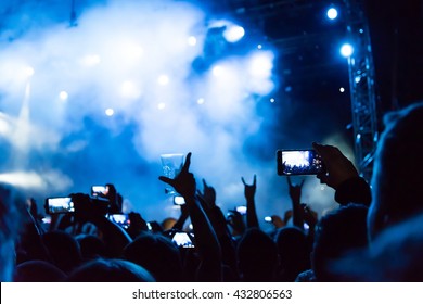 Rock Concert, Silhouettes Of Happy People Raising Up Hands In Front Of Bright Stage Lights. Space In Left Side