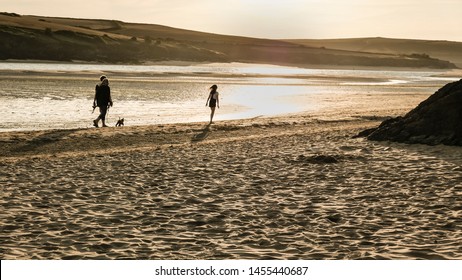 Rock, Cornwall, England UK - 07.12.2019: A Family Of Three And A Dog Walking Along The Seashore With The Evening Sun On The Camel Estuary At Low Tide In North Cornwall.