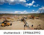 Rock crushing plant. Gravel separation machine. Construction materials production. Yellow tractor left, scenic landscape. Green hills, blue sky and clouds. Almaty region, Kazakhstan