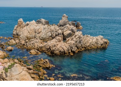 Rock Formations In Ocean Cove Near Craggy Coastline With Ships On Horizon.