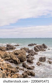 Rock Formations In Ocean Cove Near Craggy Coastline With Ships On Horizon.